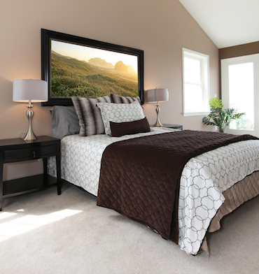 a carpeted room with a high sloping ceiling, two small bright windows, and a two-person bed with a bedside table and a lamp on each side