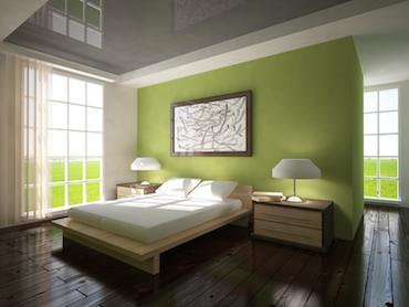 a room with a hardwood floor, bright windows on two sides, and a two-person bed with a bedside table and a lamp on each side